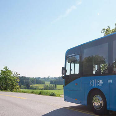 HRT:s blå buss ute på landsbygden i soligt sommarväder.