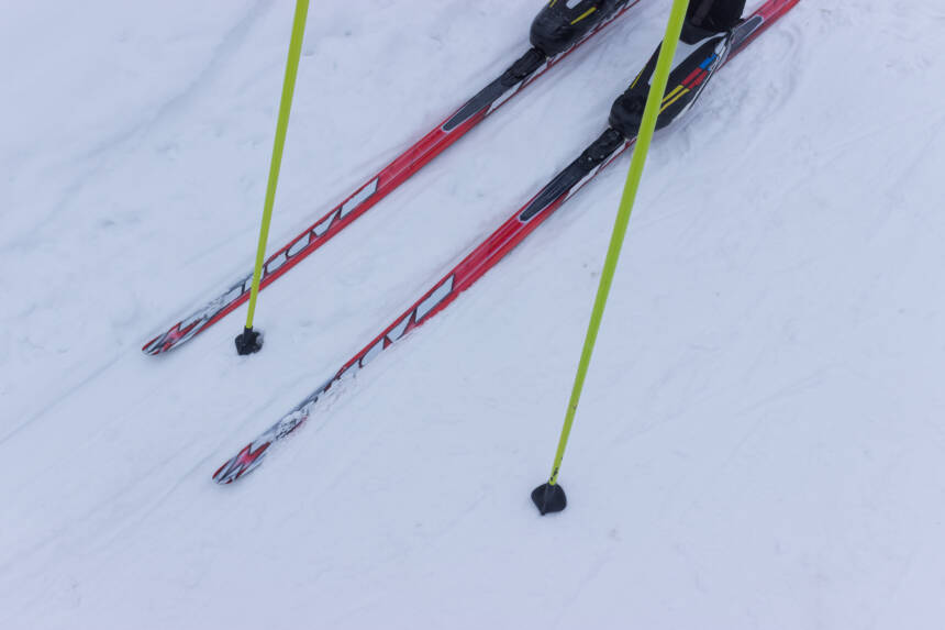 Någon står på röda skidor i snön och håller i gula stavar.