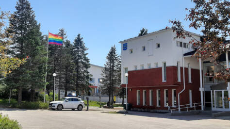 Kommunhuset i solsken sommardag med regnbågsflaggen hissad i flaggstången.