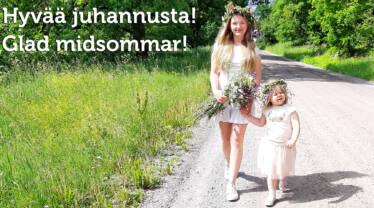 En tonårig flicka och en liten flicka med blomkransar i håret går på en grusväg. Bilden har texten Glad midsommar.