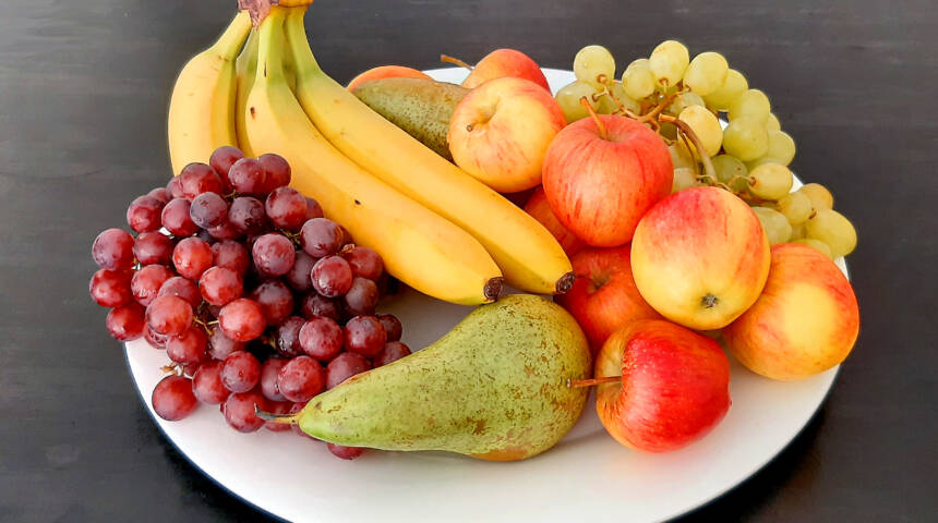 Banaaneja, viinirypäleitä, omenia ja päärynöitä isolla lautasella.