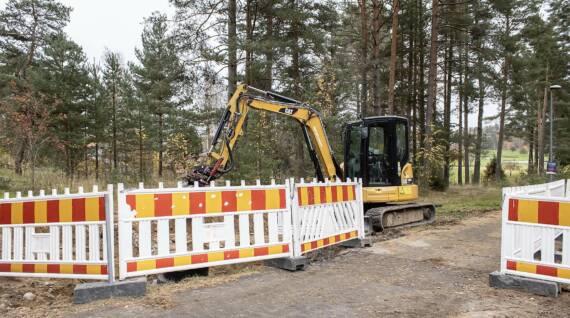 Pieni kaivinkone pysäköitynä työmaaksi aidatulla alueella.